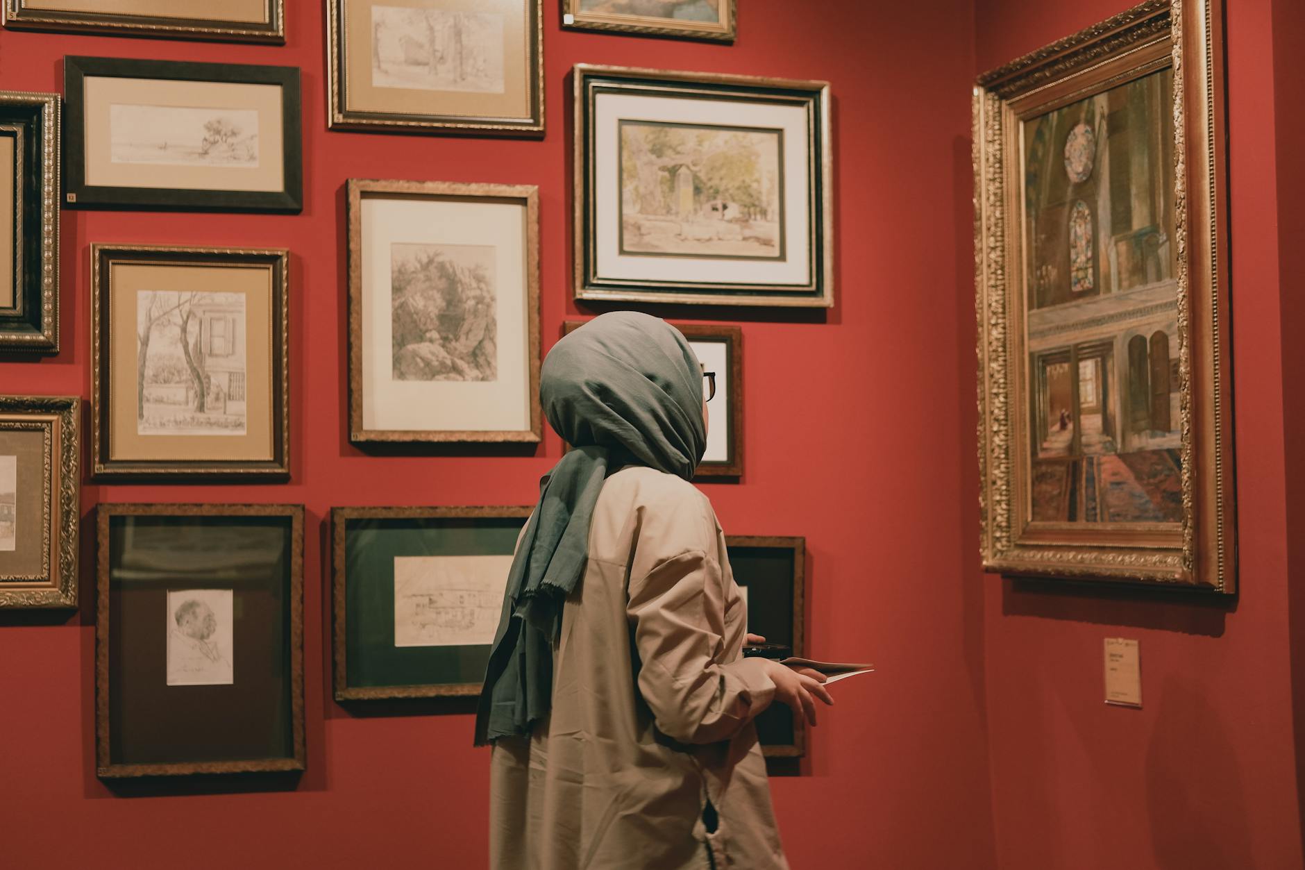 A woman observing paintings in a red-walled art gallery