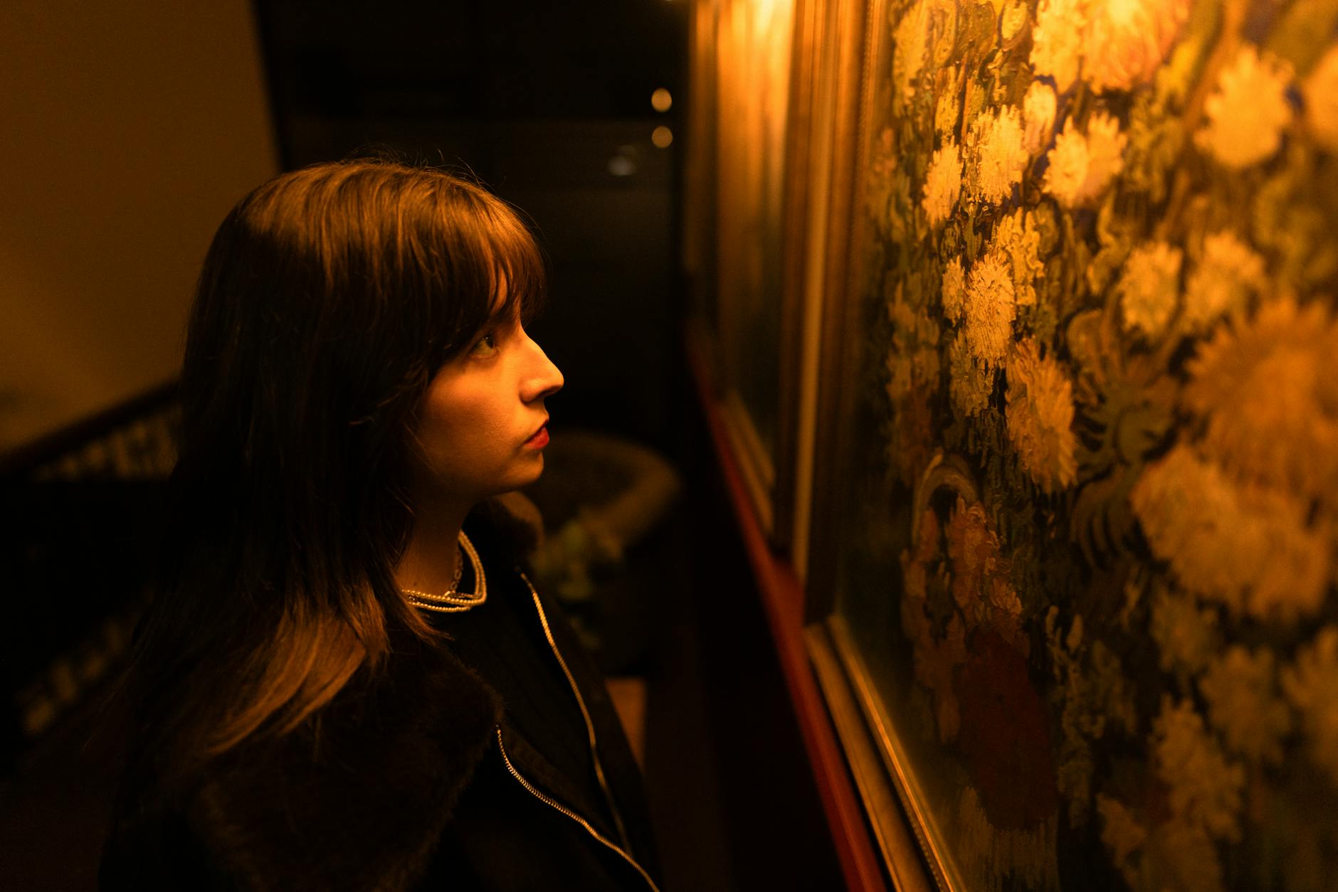 A young woman deeply engrossed in viewing paintings in a warmly lit art gallery