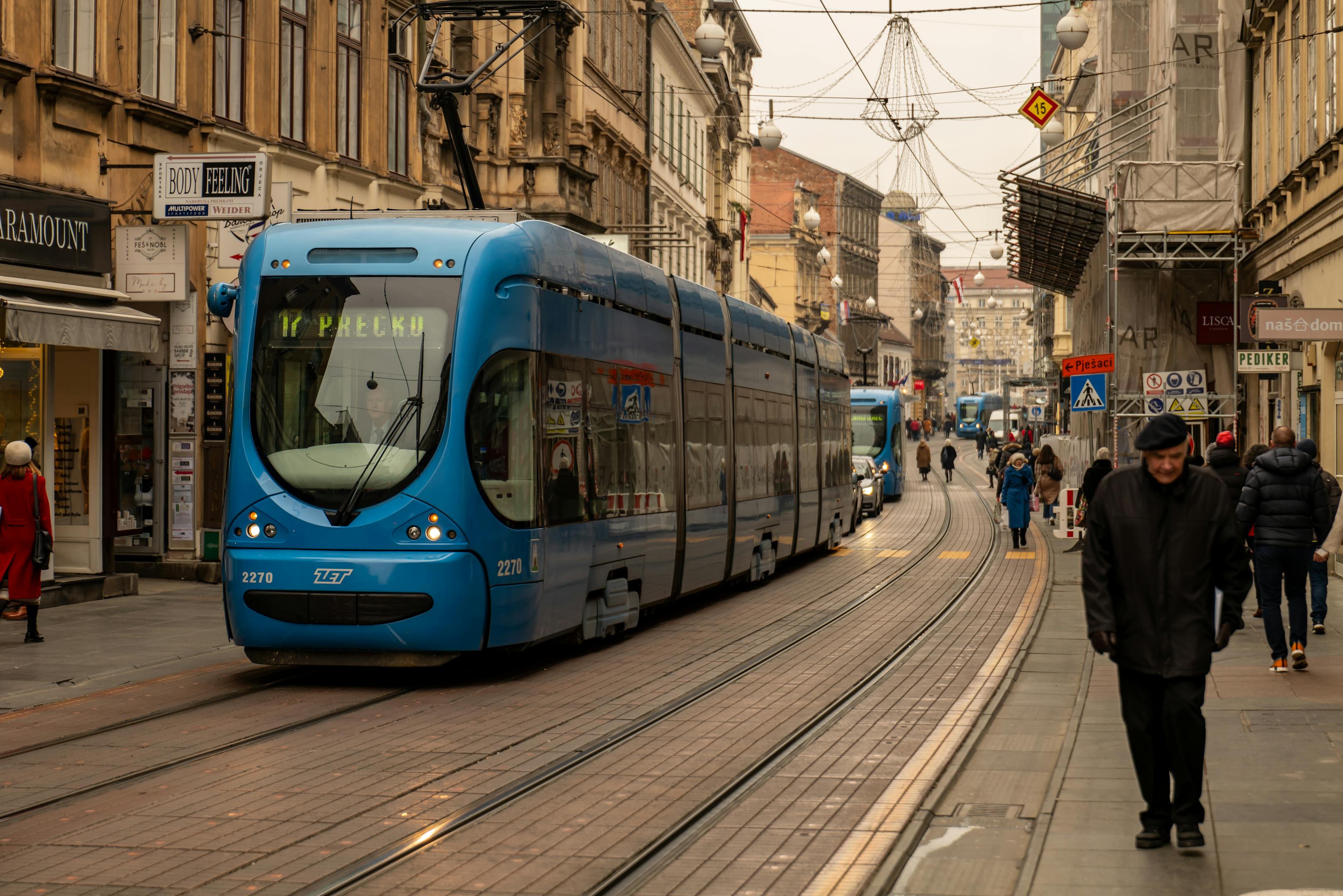 A blue tram travels through a bustling street in Zagreb, Croatia's capital city