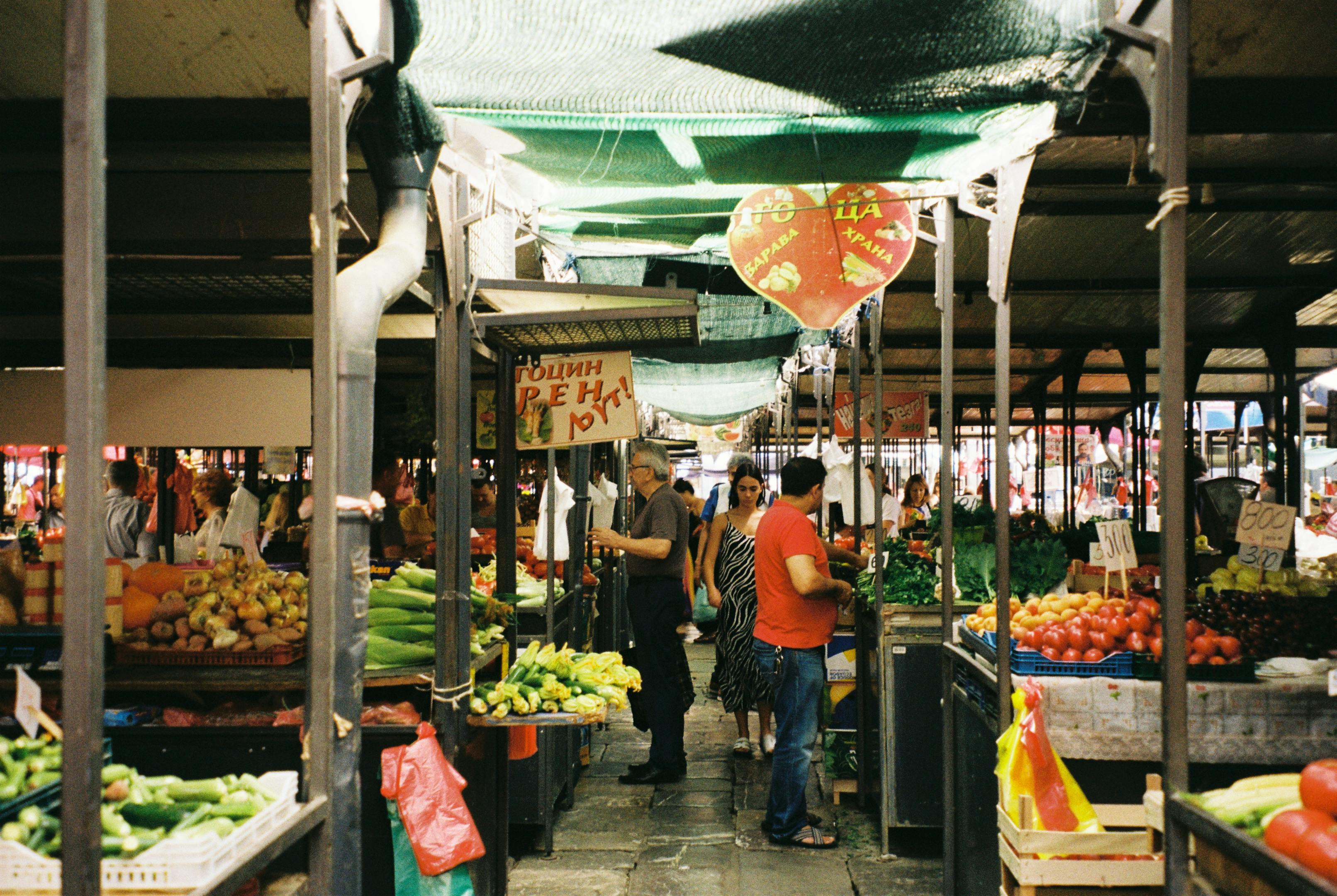 A bustling outdoor farmer's market with fresh vegetables and people shopping on a sunny day